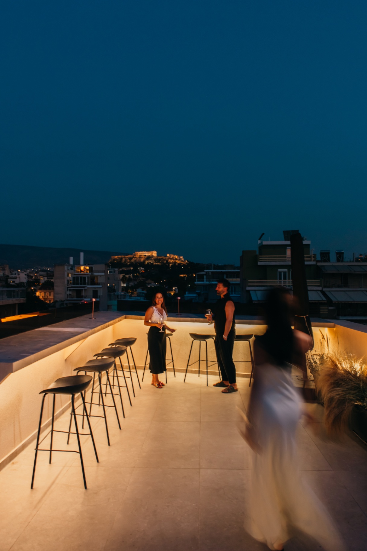 Warmly-lit rooftop bar with stools at night