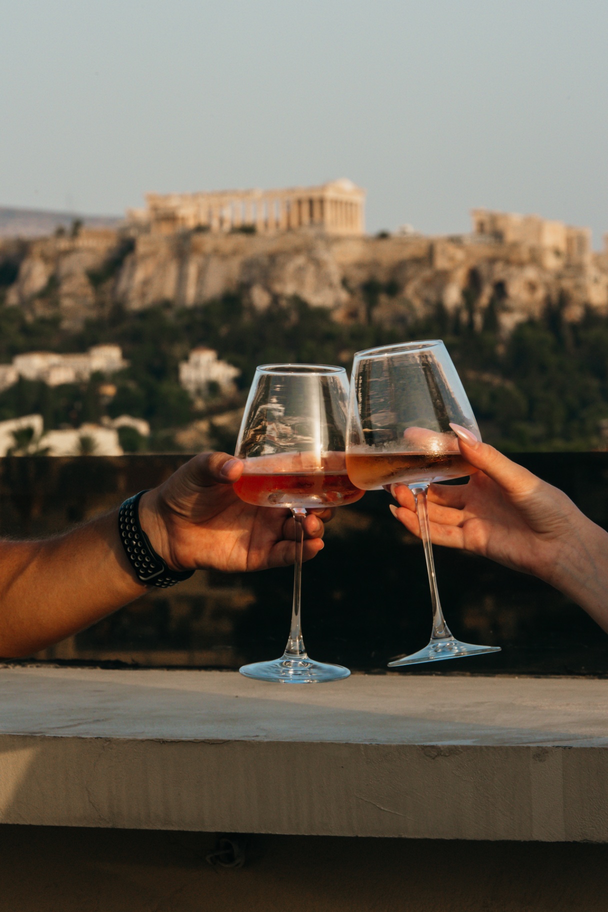 Guests raising rosé glasses in the golden light with the Acropolis behind