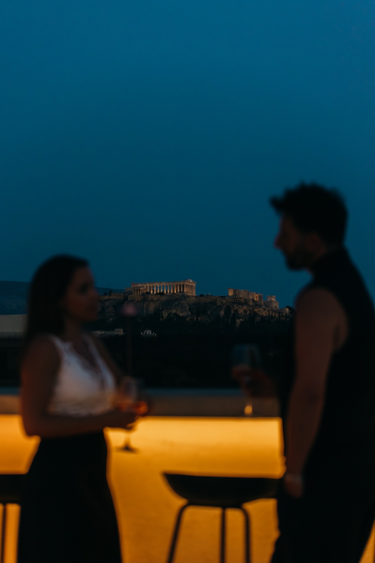 Two friends in silhouette on the rooftop with the lit Acropolis